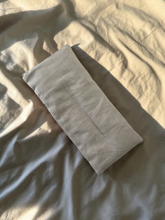 Coussin Morphée gris clair en lin lavé, posé sur la literie, lumière naturelle